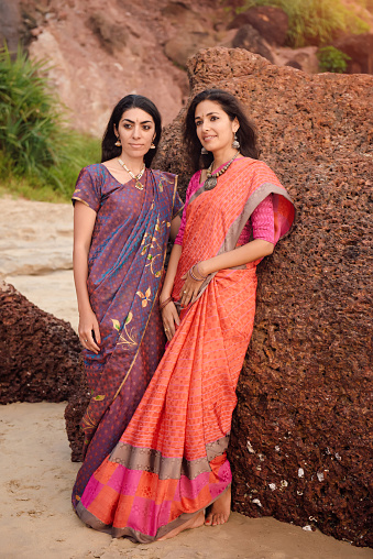 Fashion shoot of indian woman in traditional clothes. Friends girl in beautiful saree standing on the rock near the sea in saree at sunset